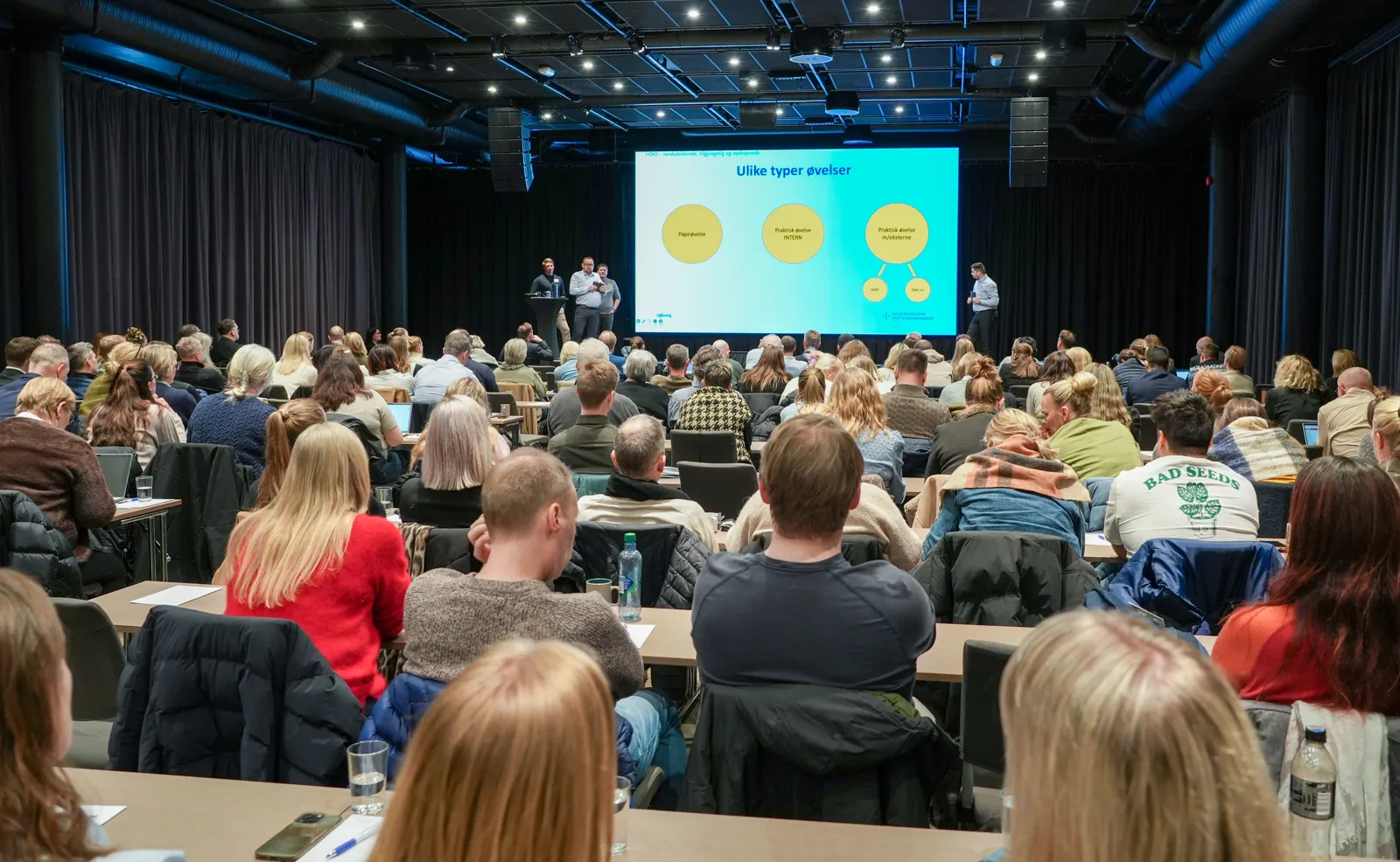 En gruppe mennesker som sitter i et rom med en stor skjerm