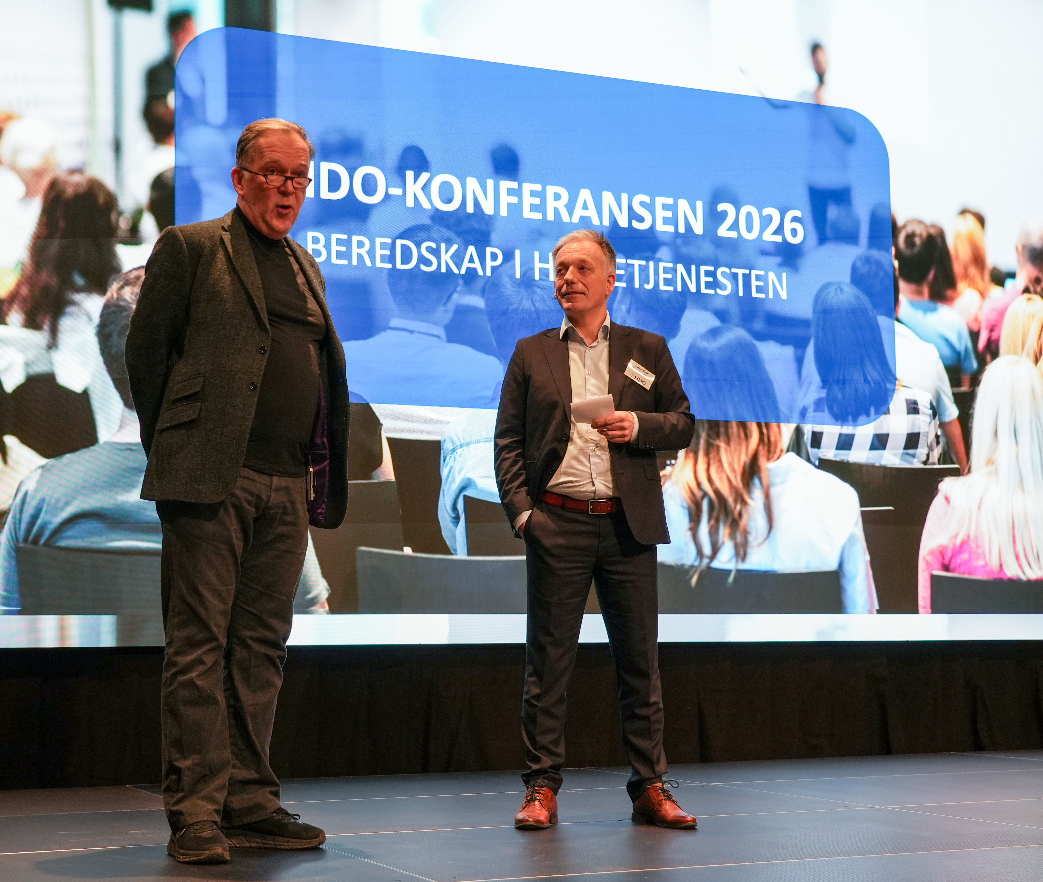 Et par menn som står på en scene med en stor skjerm bak seg