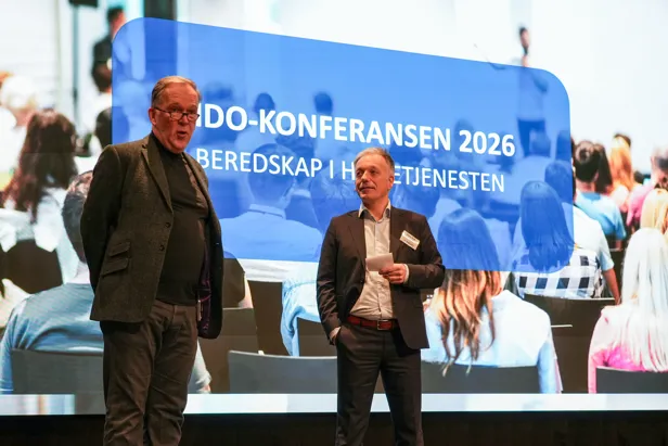 Et par menn som står på en scene med en stor skjerm bak seg