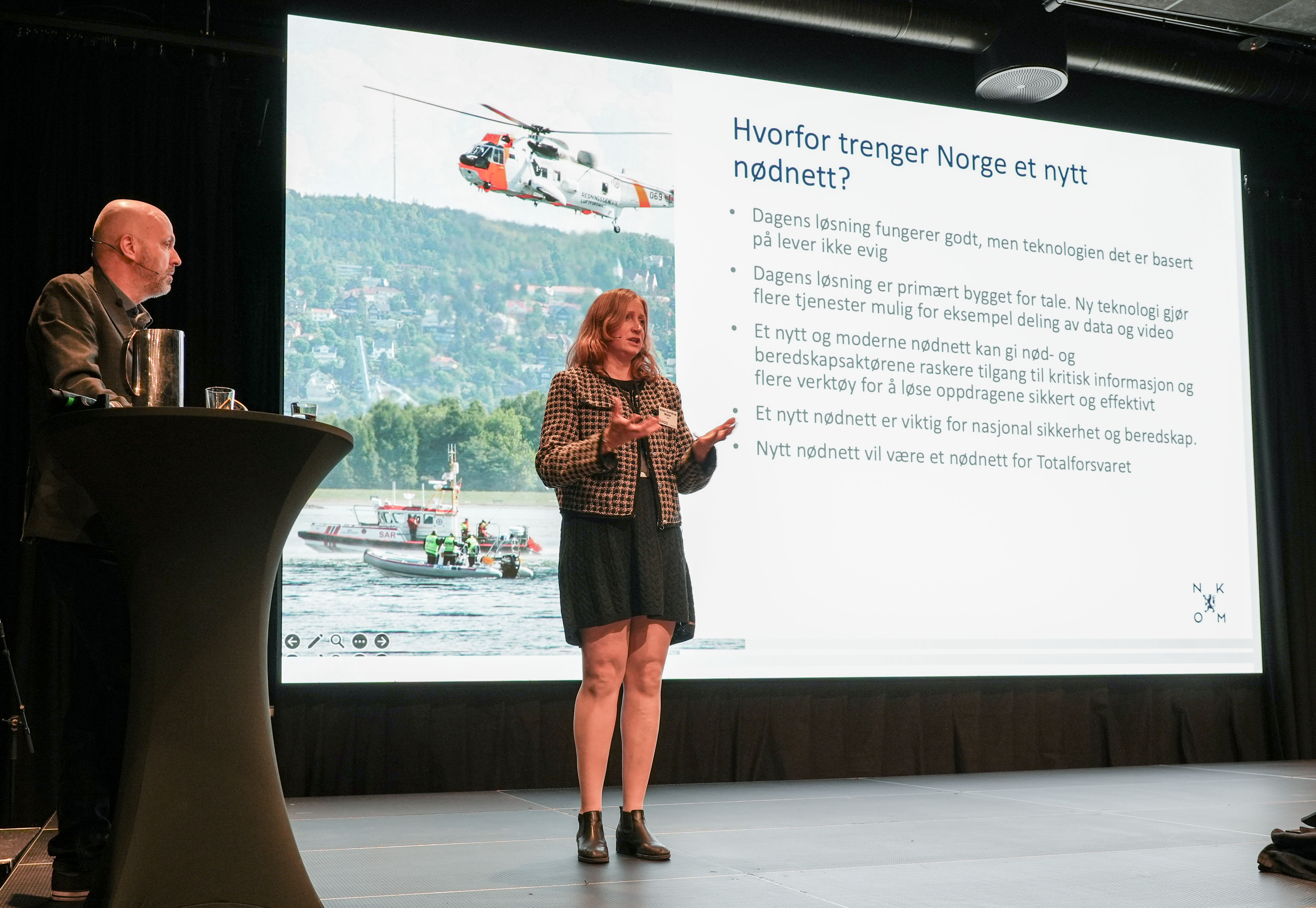 En kvinne som står foran en skjerm med en mann som sitter ved en talerstol