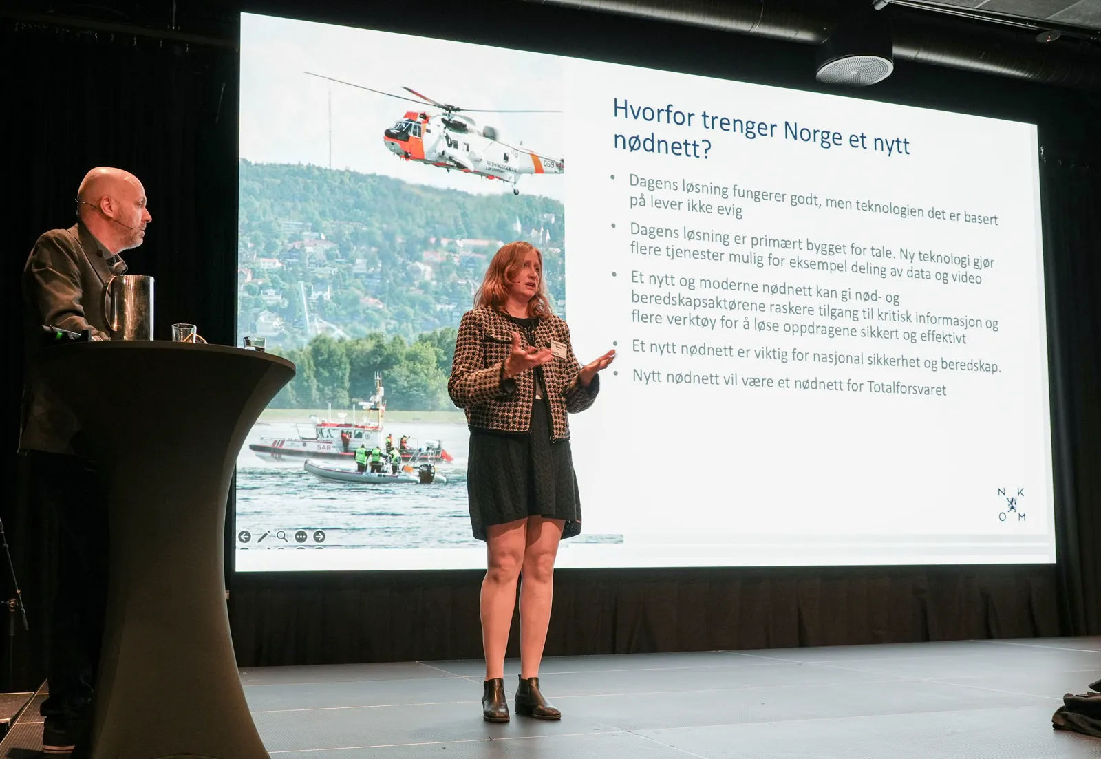 En kvinne som står foran en skjerm med en mann som sitter ved en talerstol