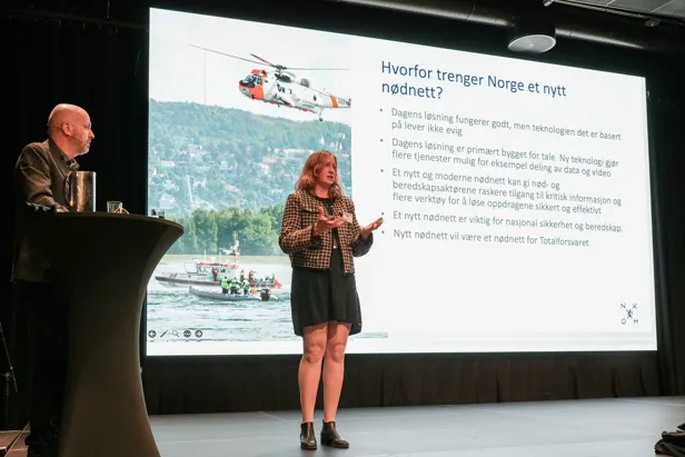 En kvinne som står foran en skjerm med en mann som sitter ved en talerstol