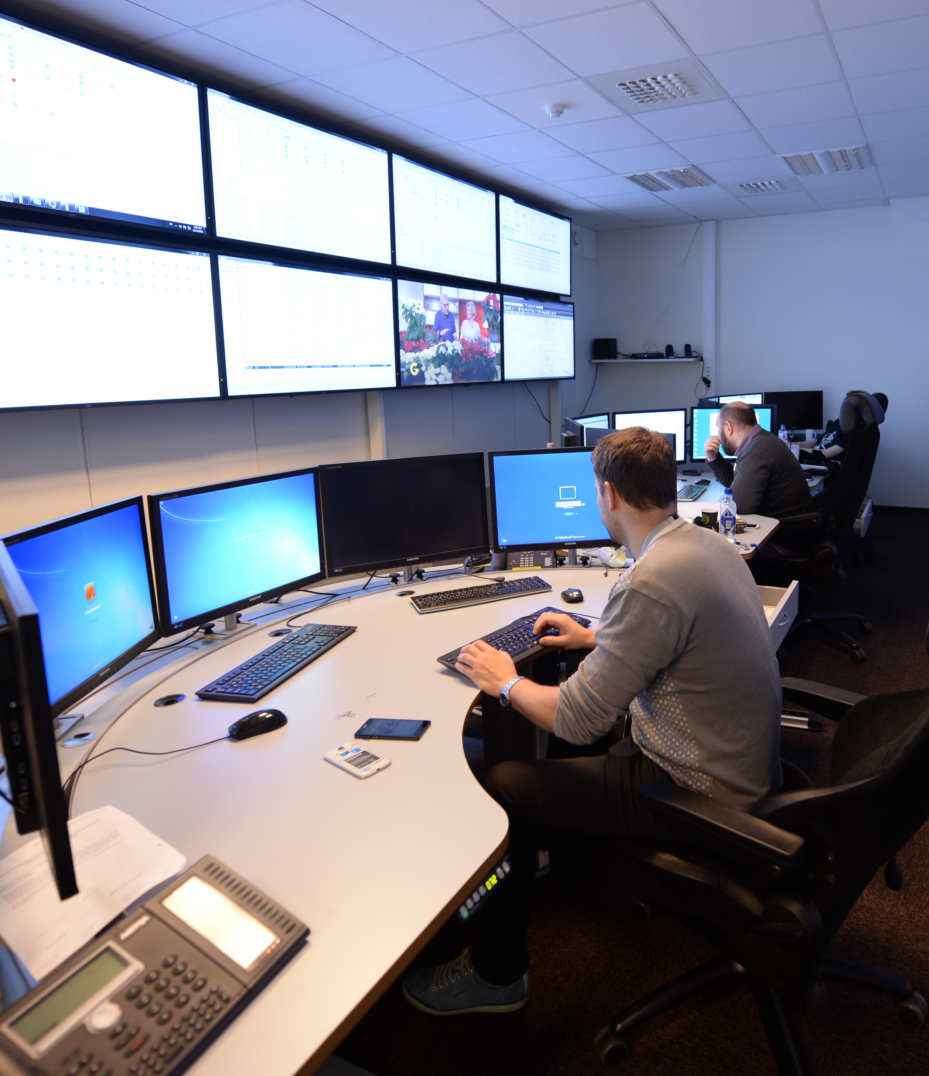 bilde av to mennesker som sitter på kontoret ved hver sin pult med mange skjermer