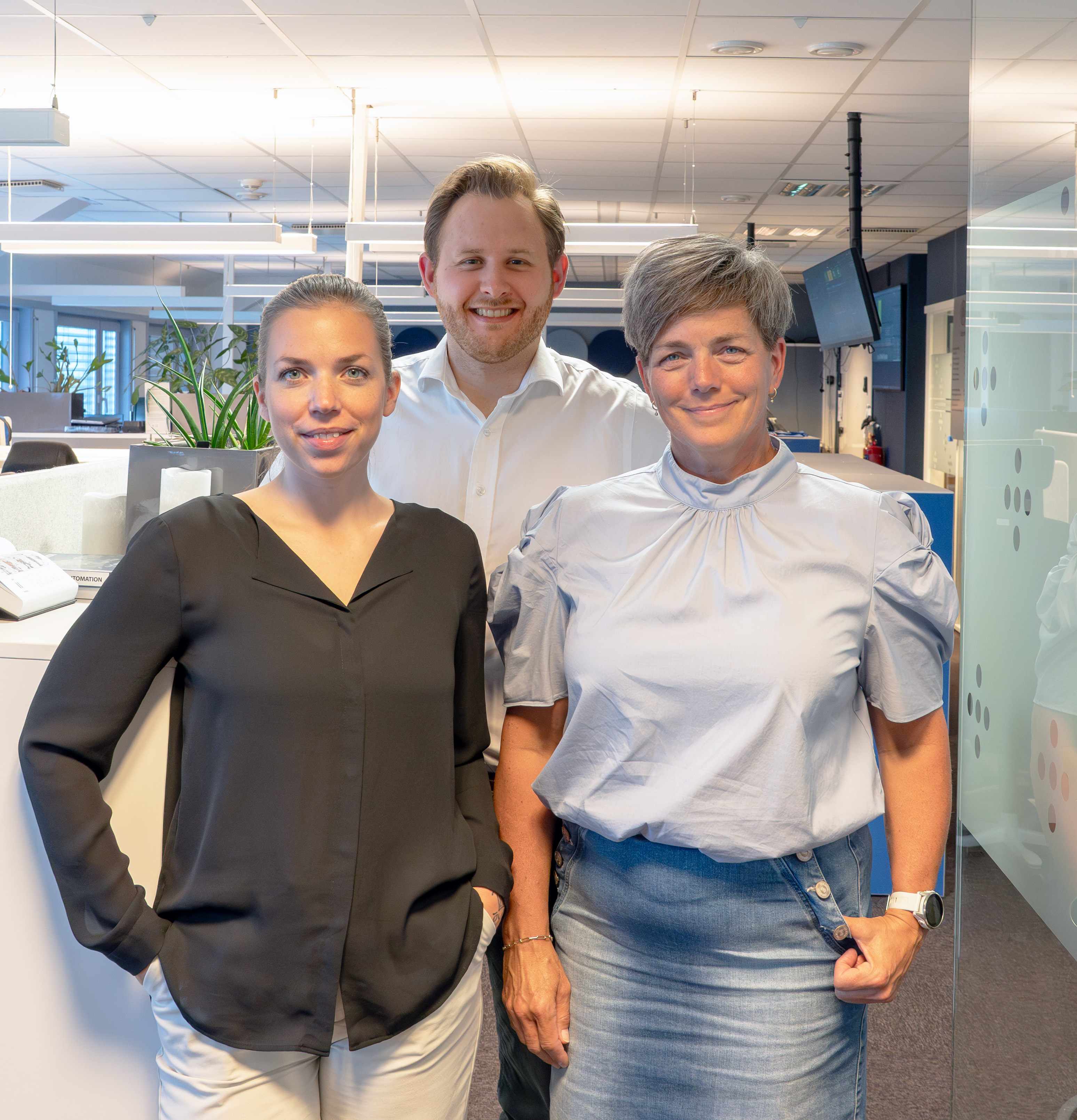Tre personer som står i et åpent kontorlandskap