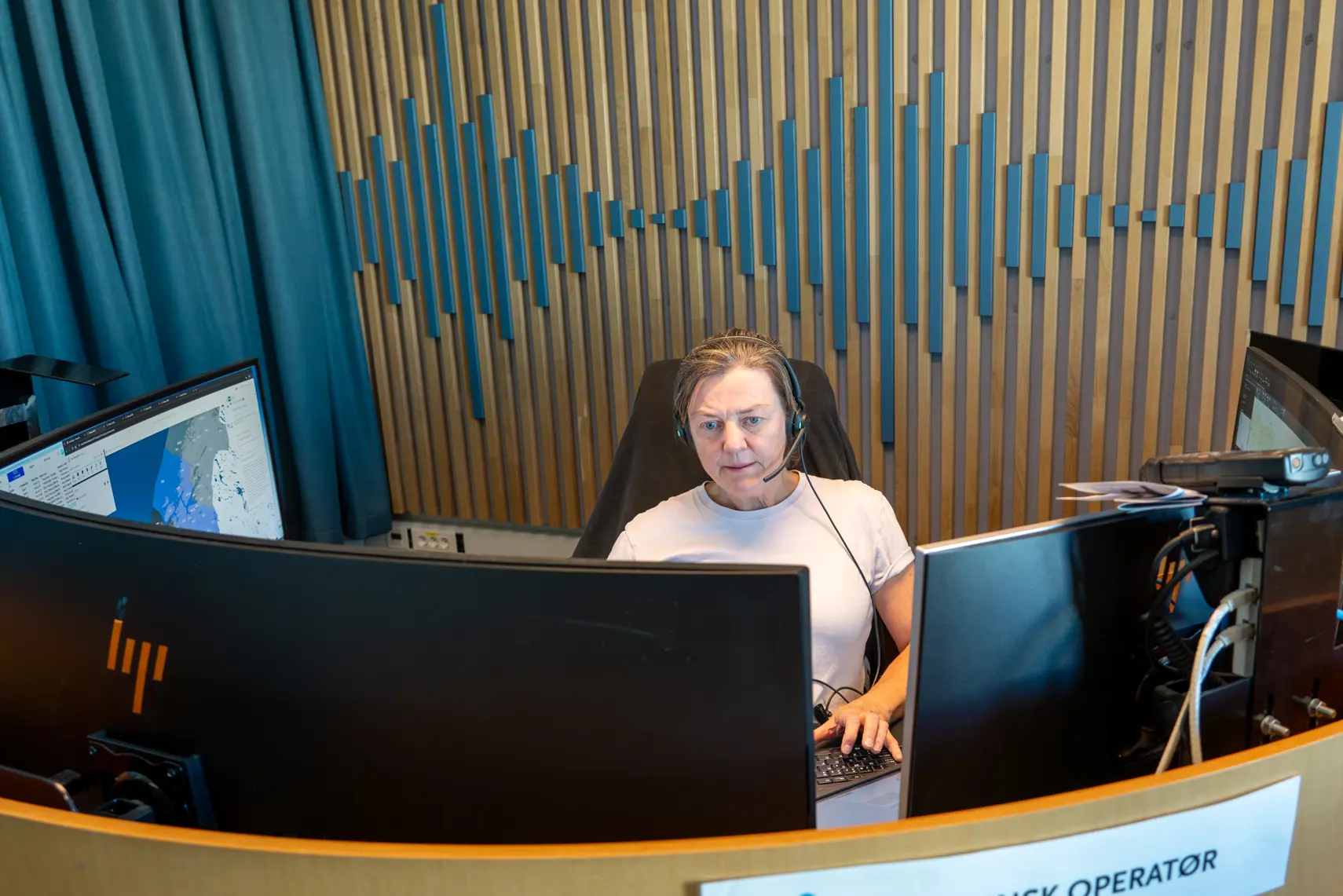 En person som sitter ved et skrivebord med en bærbar datamaskin og andre datamaskiner